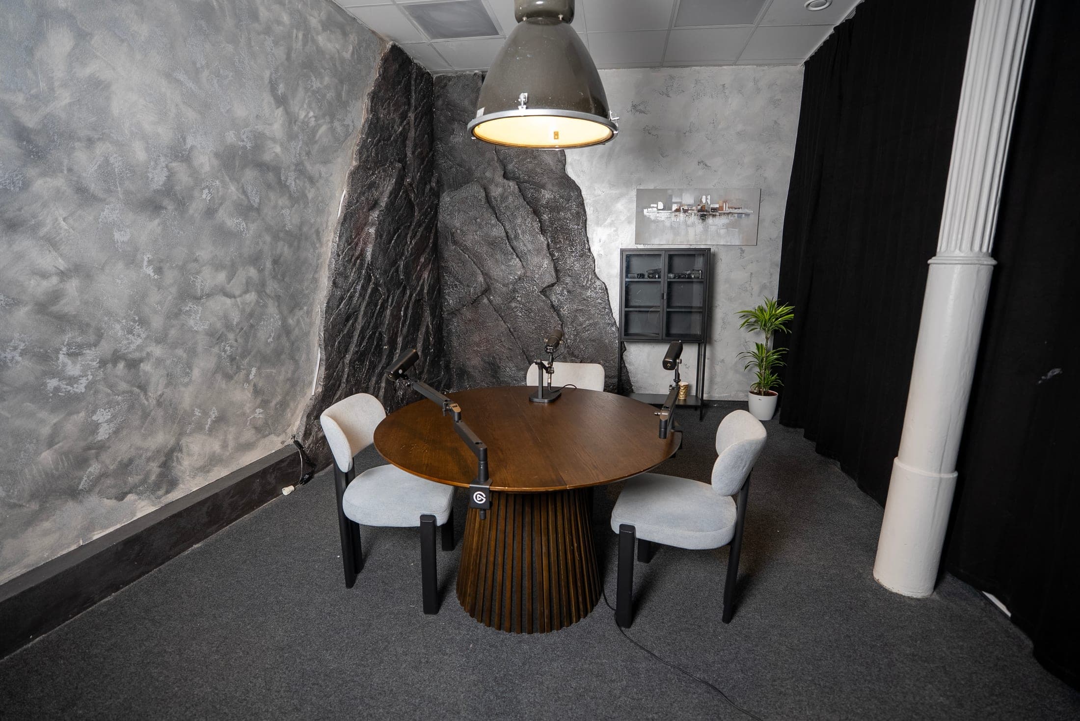 Podcast Room mit rundem Tisch, Mikrofonen und Steinwand